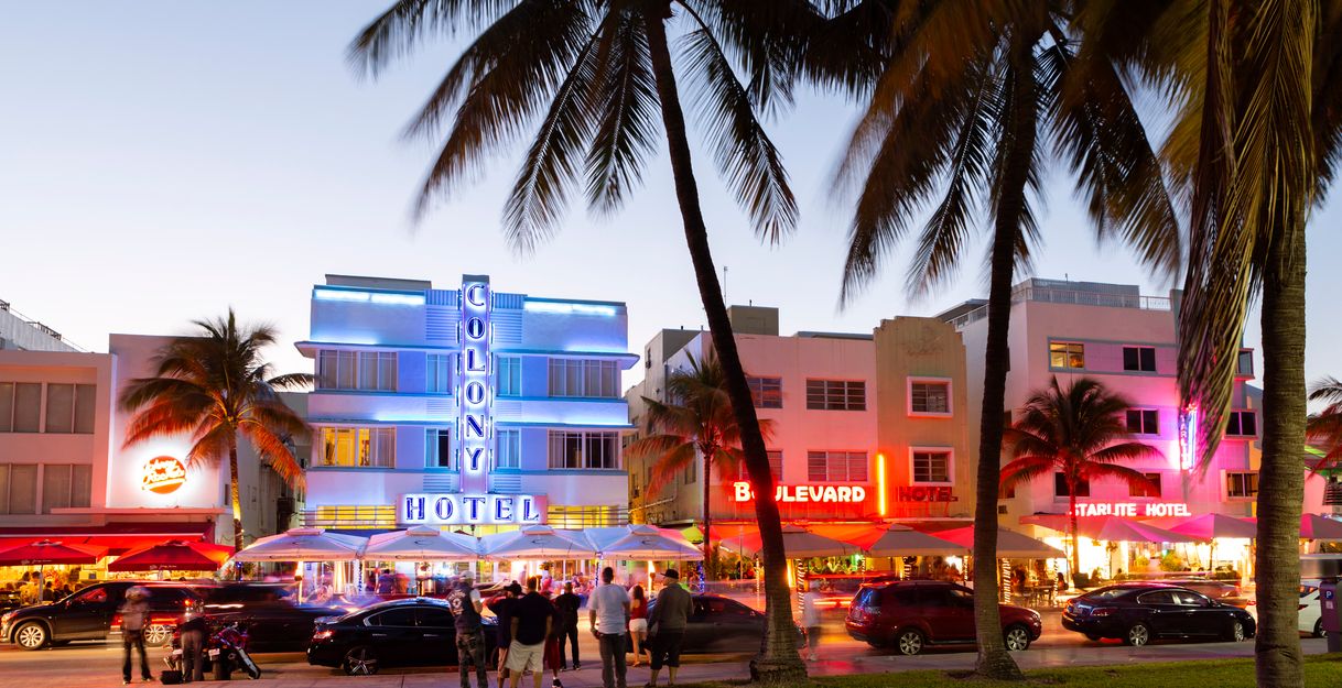 Das Bild zeigt den Ocean Drive in Southbeach Miami im Abendlicht mit leuchtenden Neon-Schildern. 