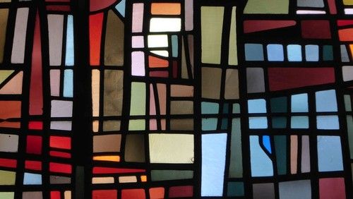 Buntes Kirchenfenster mit abstraktem Design aus verschiedenen farbigen Glasstücken.